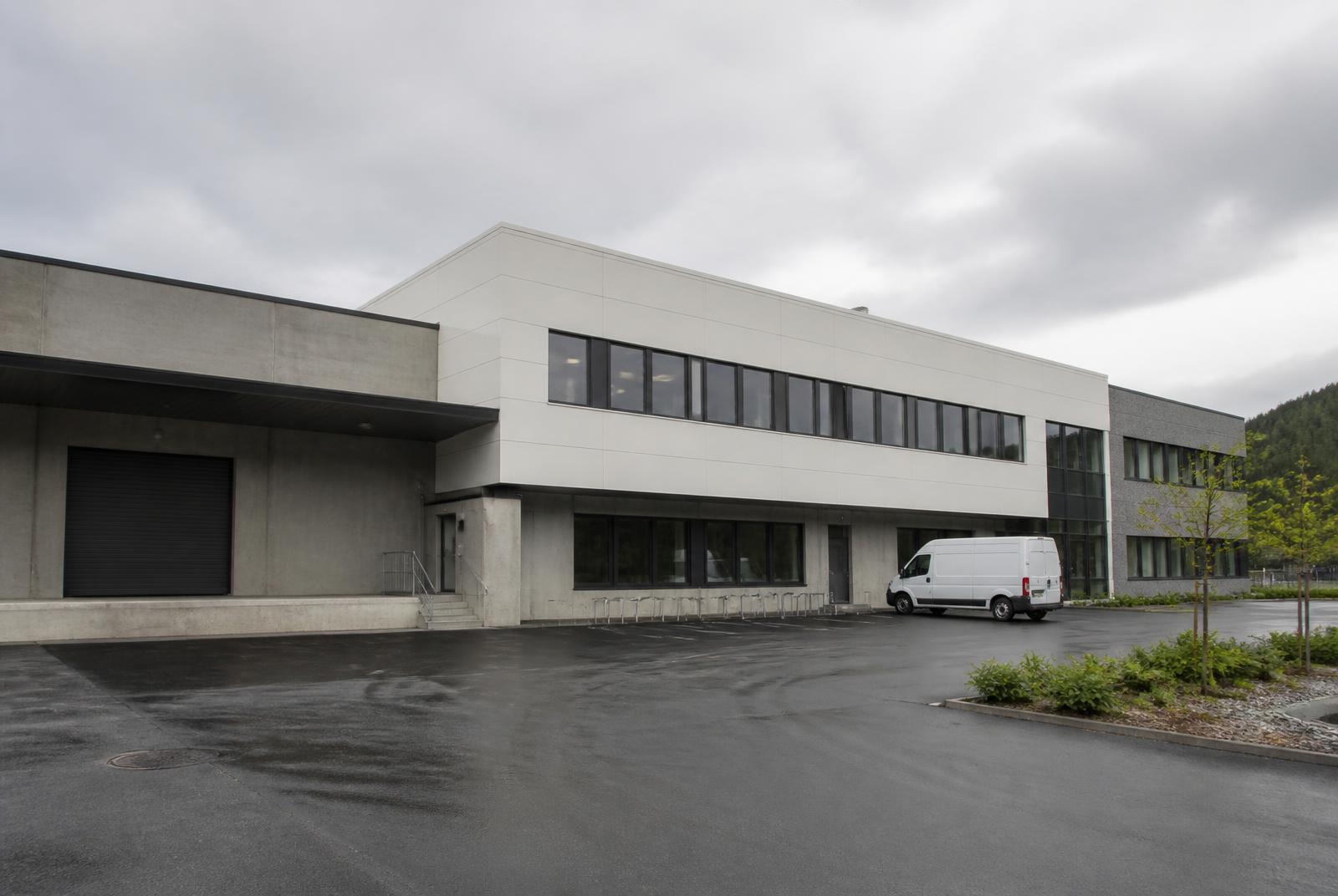 Moderne næringsbygg med port, vareinngang og stort asfaltert uteareal langs regional vei, illustrerer virksomhetslokaler i E6-korridoren ved Halden