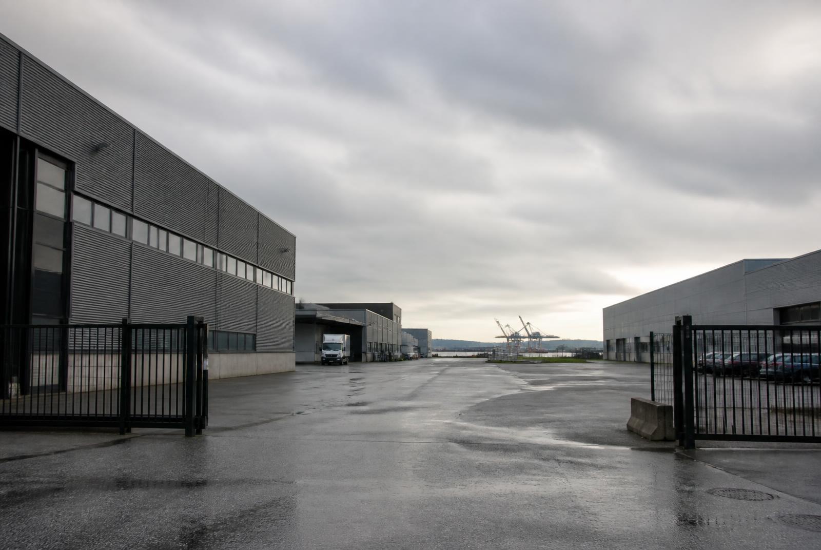 Større nærings- og industriområde ved havn med porter, asfaltert gårdsplass og lastebil ved lasterampe, illustrasjon til virksomhetsflytting på Øra i Fredrikstad